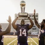 Bo Nix celebrates with trophy alongside brothers doing high-five with blurred stadium lights behind