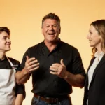 Bobby Flay talking with young chef and food critic while gesturing with kitchen utensils showing dream hosts