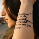 Brianna shows faded Heart of Dixie tattoo on forearm with golden sunset and blurred rural town behind