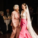 Bride revealing bright pink lace jumpsuit to smiling aunt at wedding reception with soft lighting highlighting their joy
