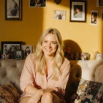 Brittany Snow sits on plush couch with nostalgic photos and golden light showing her wistful smile