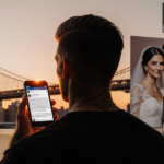 Brooklyn Beckham holding a phone with an Instagram screenshot backlit by a sunset over Brooklyn Bridge