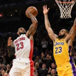 Cade Cunningham driving to the hoop with LeBron James in passing while Luka Doncic guards him and the crowd cheering