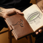 Carlos Alcaraz holds a leather book with a kangaroo cover and an illustration of the Sydney Cricket Ground in golden light.