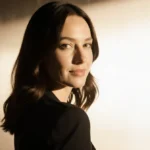 Carrie Coon turns to camera with introspective gaze and golden background highlighting her sharp features