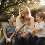 Carrie Underwood sits on wooden bench with her laughing sons and baseball bat while sunlight filters through backyard trees