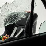 Empty child car seat reflecting shattered windshield with a lone toy beside it and soft light illuminating the sterile white