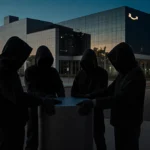 Four hooded figures gripping a large cylinder with streetlights and a dusk logistics center behind them