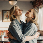 Claire Danes and Amy Poehler embrace holding hands with warm 1990s diner backdrop and natural light.
