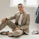 Hands smooth tailored pants with sneakers and denim jacket nearby on minimalist surface