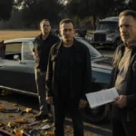 Three men examine a vintage car with concern while holding an inspection manual and tools beside the open hood