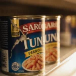 Tuna cans scattered across grocery shelf with torn label and dented can showing contamination concern