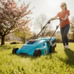 Person mowing lush green lawn with bright blue cordless electric mower and blooming flowers in warm sunlight
