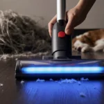 Hand guides cordless vacuum with blue light bar across dark hardwood floor showing clean trail and pet hair mess