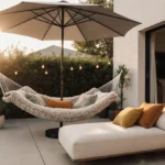 Plush hammock and chaise lounge sit on cozy patio with umbrella shade and potted plants nearby