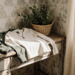 Neatly folded long‑sleeve tops lie on a vintage wooden desk with warm golden light streaming in during a cozy spring morning.