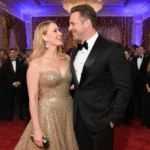 Dax Shepard and Kristen Bell gazing at each other on the red carpet with Kristen wearing gold gown and Beverly Hilton ballroo