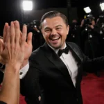 Leonardo DiCaprio laughing and high-fiving friends at Golden Globes with flashing camera lights illuminating his joyful expre