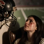 Woman weeping in armchair with cracked football helmet on wall and faded gridiron pattern behind