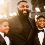 DJ Khaled stands proudly on the Grammy Awards red carpet with his family and two sons wearing tuxedos and smiles.