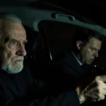 Elderly man pointing gun at cowering Uber driver with stark dashboard lighting creating menacing shadows