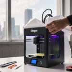 Person unboxing compact Elegoo 3D printer with hands revealing sleek design and colorful accents at desk