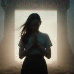 Eleven standing alone with hands clasped and faint portal glow behind her in the Upside Down landscape