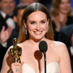 Erin Doherty holds Golden Globe award with censored word near microphone and cheering crowd behind