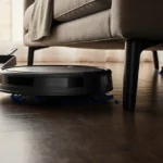 Eufy 11S Max robot vacuum gliding under couch with spinning brushes and cleaning supplies on dark hardwood floor