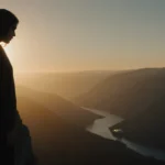 Woman standing on cliff edge looking down at valley with misty golden car in background