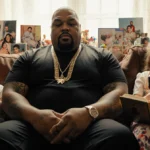Fat Joe sits on couch with family photos of his children and music memorabilia lighting the warm room.