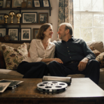 Amy Madigan and Ed Harris laughing together on a couch with warm natural light and family photos.
