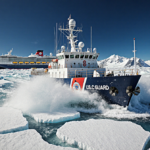 Coast Guard cutter breaking through ice with foam plumes and a trapped cruise ship in Antarctica.