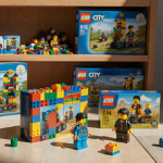 Lego figures building on a colorful table with scattered pieces and bright colors on a neutral floor.