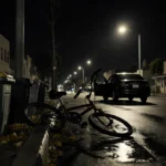 Abandoned bicycle lies on wet pavement with streetlight shadows in nighttime Pacific Beach cityscape