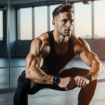 Fitness enthusiast squatting with smart wearables and wrist tracker against energetic studio mirrors.