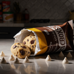 Frozen cookie dough bag knocked over spilling white chocolate chips with golden light on kitchen counter