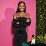 Gabrielle Union stands confidently with arms crossed against a pink Met Gala backdrop wearing a sleek black gown with gold ac
