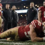 George Kittle clutching his ankle in pain with Brock Purdy watching and concerned teammates gathering around