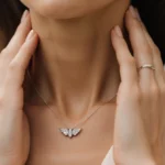 Gisele Bündchen cradles her neck with elegant hands and a delicate diamond wing necklace sparkling in soft light