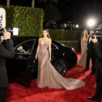 Starlet stepping onto Golden Globes 2026 red carpet with shimmering gown and paparazzi flash