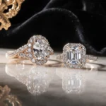 Two antique engagement rings sparkle on white marble with black velvet and gold filigree framing