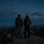 Hikers standing at summit with indigo sky and abandoned backpack near rocky terrain.