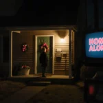Suburban porch light glowing warmly on front door with Home Alone TV reflection showing in window