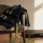 Weighted vest draped on armchair with resistance bands tangled around legs and under-desk walking pad humming nearby