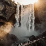 Horsetail Fall cascades down rocky cliffs with golden sunrise light illuminating mist and tourists watching in awe