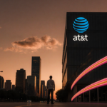 Person standing in front of sleek building with orange‑pink fiber‑optic cable and AT&T logo as dusk sky glows