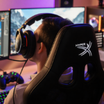 Person sitting and gaming with HyperX Cloud Flight headset and multi-monitor setup under warm lighting