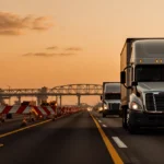 Truck driving slowly with frustrated driver near orange cone blocking lane under warm sunset sky