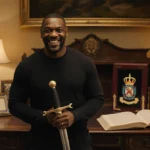Idris Elba smiling warmly while holding the Royal Sword with royal awards and leather book on wooden desk
